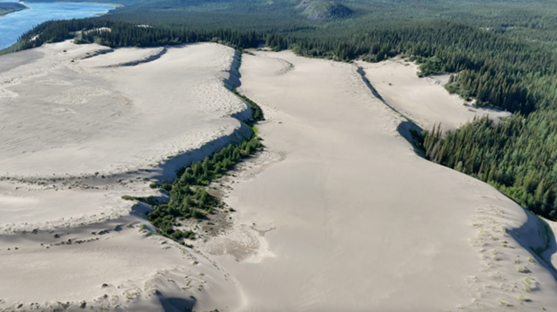 Vue aérienne panoramique de grandes dunes bordées d’arbres à feuilles persistantes. Carte de la région (Geo.ca).
