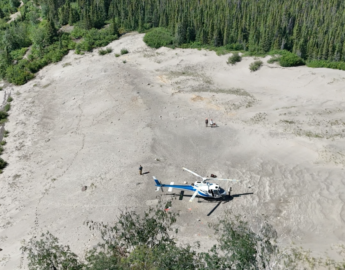Vue aérienne d’un hélicoptère posé sur une dune, avec quelques personnes aux alentours qui étudient la surface.