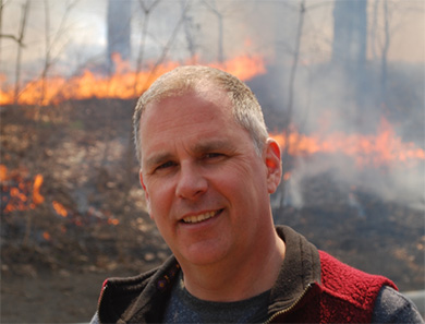 Mike Wotton, devant un feu de forêt qui brûle à l’arrière-plan.