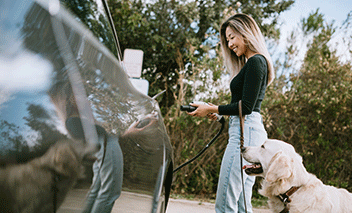 A young woman charges her electric car by plugging it in at a power source parking spot.