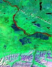 L'image montre une prédominance de vert avec des teintes de rouge visibles dans les cours d'eau chargés de sédiments