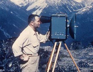 Technicien qui regarde à travers d’un telluromètre sur un trépied avec des montagnes dans l’arrière-plan.
