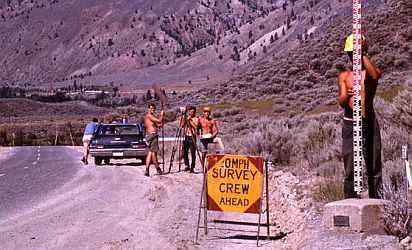 Des techniciens qui prennent des mesures de nivellement sur le côté de la route avec un panneau indiquant 0MPH Survey Crew Ahead
