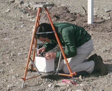 Technicien à genou sur le sol rocheux en train de prendre des mesures avec un gravimètre Lacoste-Romberg