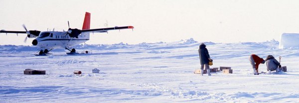 Technicien qui travaille avec de l’équipement sur la neige avec un avion dans l’arrière-plan.