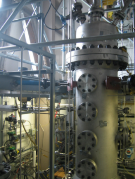 Image représentant un grand cylindre industriel en métal d’une hauteur de plus de 1,5 mètre, muni de gros boulons et de différentes jauges et connexions. 