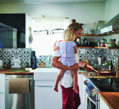 Père tenant sa fille dans ses bras pendant qu'il cuisine sur une table de cuisson électrique 