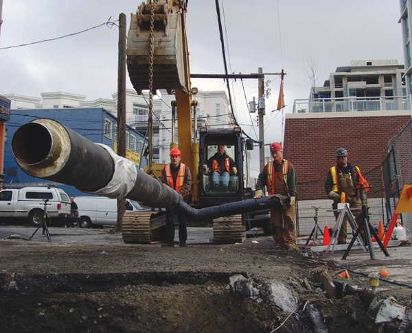 Voici une photographie de travailleurs de la construction en train d’installer les conduites de chauffage du quartier