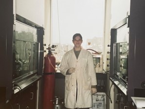 Photo d’une femme en sarrau blanc, debout dans un laboratoire et entourée d’équipements.