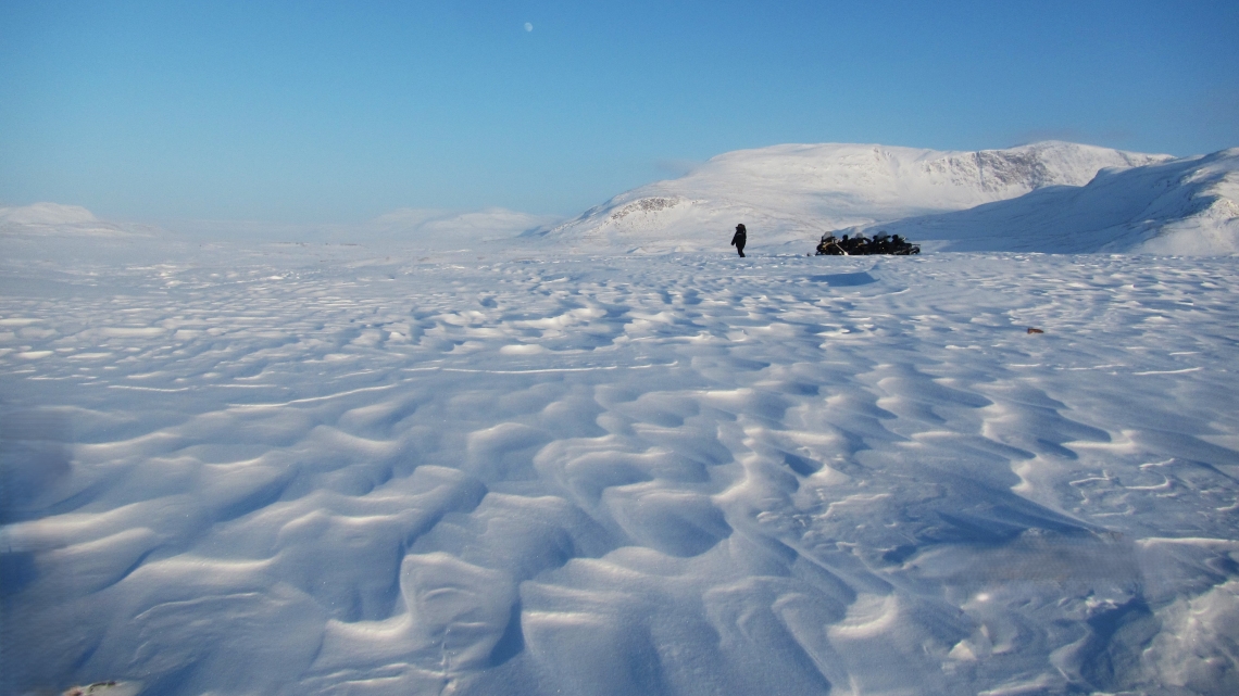 Une personne près d’une motoneige chargée d’équipement dans la toundra glacée.