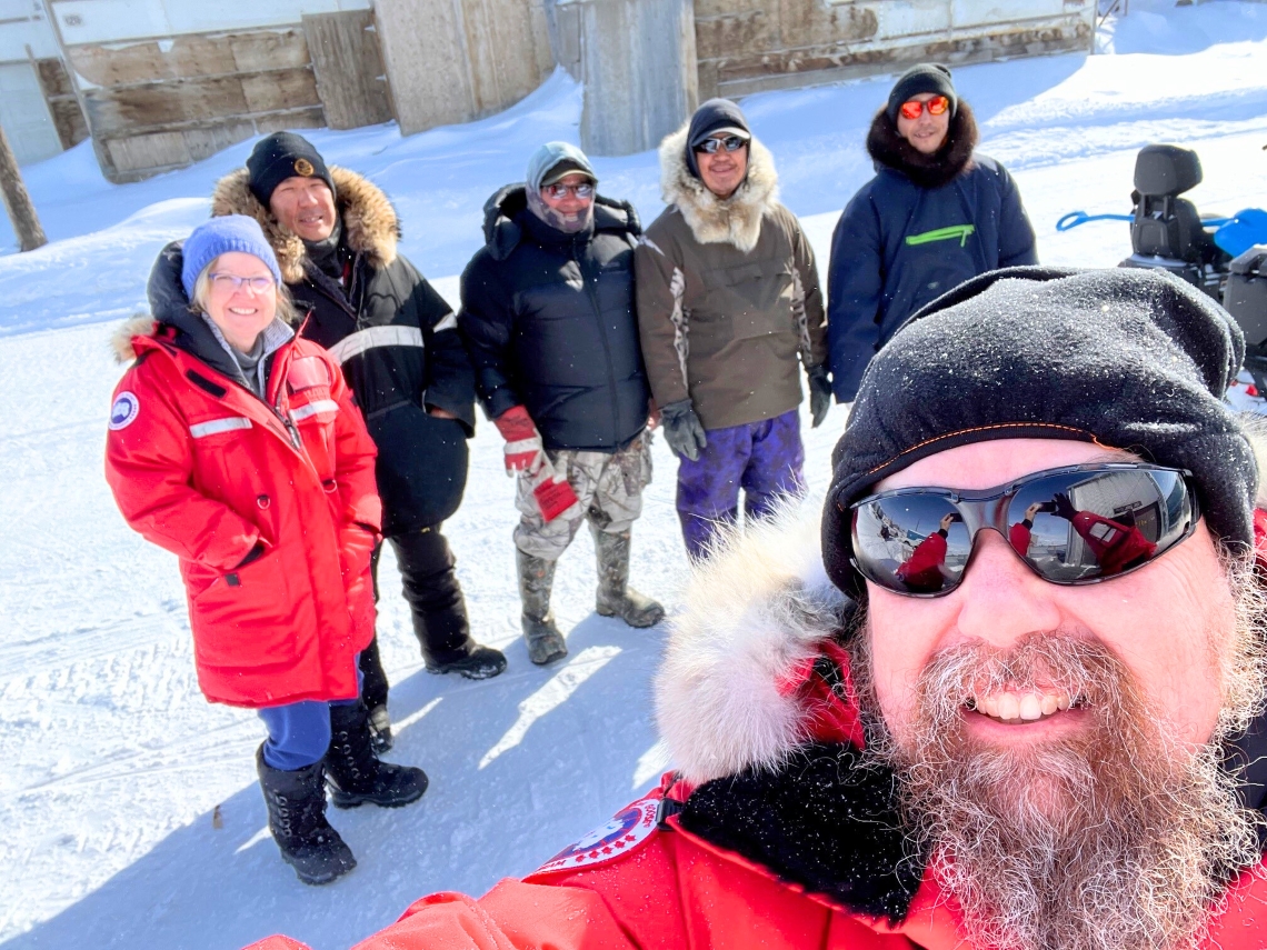 Un homme en parka rouge se prenant en photo avec une femme en parka rouge et quatre hommes en parkas à l’arrière-plan.