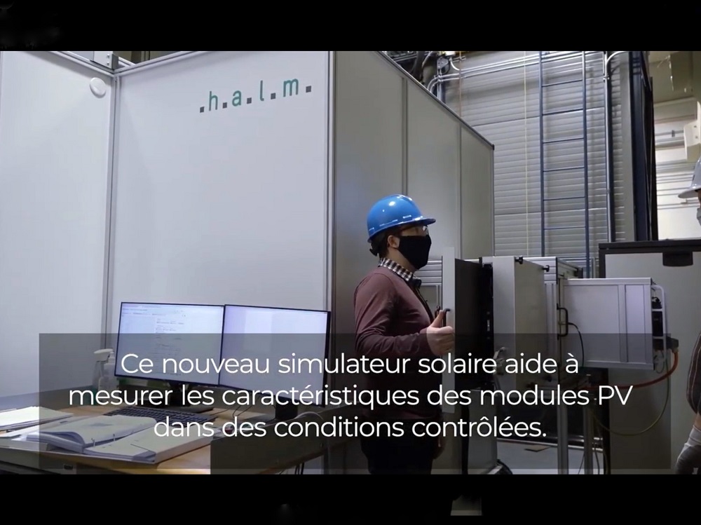 Deux hommes portant des casques de sécurité à l'extérieur d'un simulateur solaire dans un laboratoire. Texte à l'écran : Ce nouveau simulateur solaire aide à mesurer les caractéristiques des modules PV dans des conditions contrôlées.